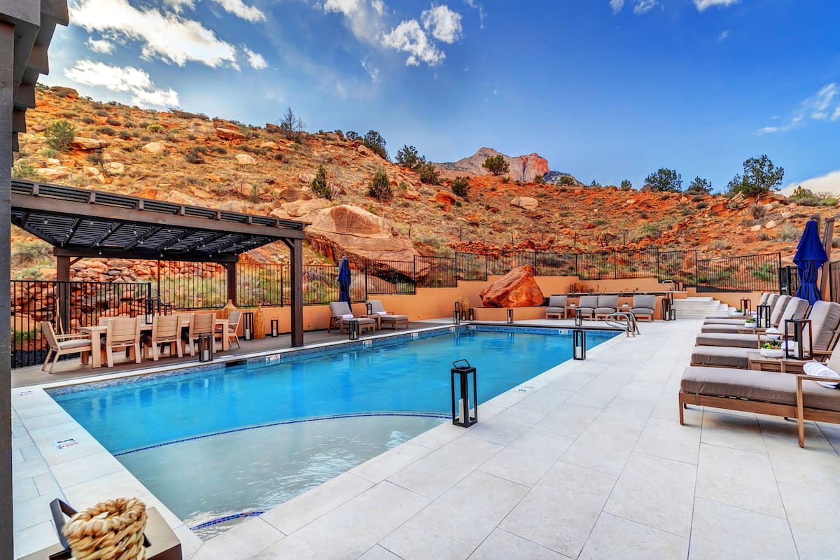 A pool area with lounge chairs and a covered seating area, surrounded by a mountainous landscape.