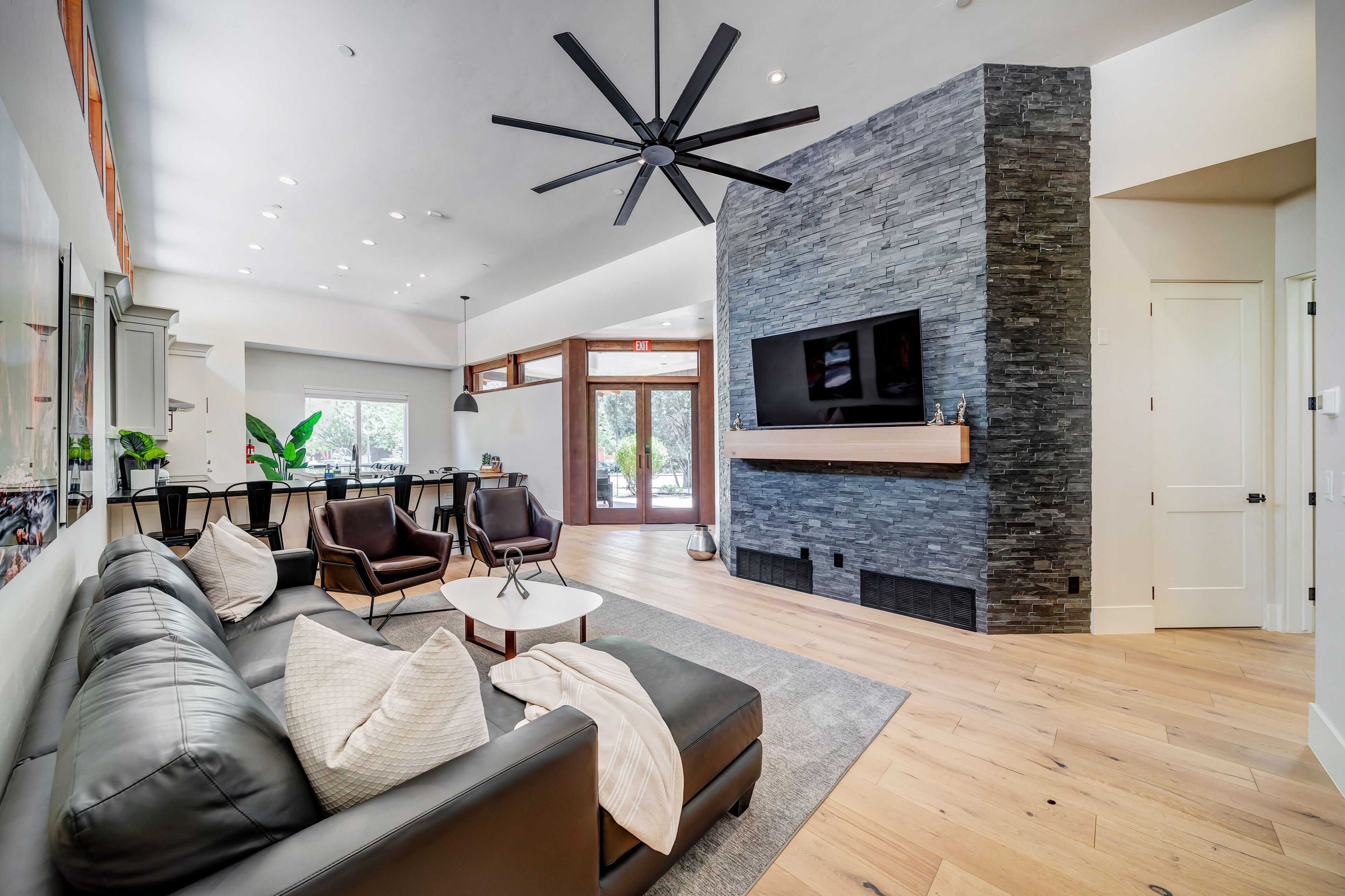 A modern living room with a black leather sofa, a stone fireplace, and a ceiling fan.