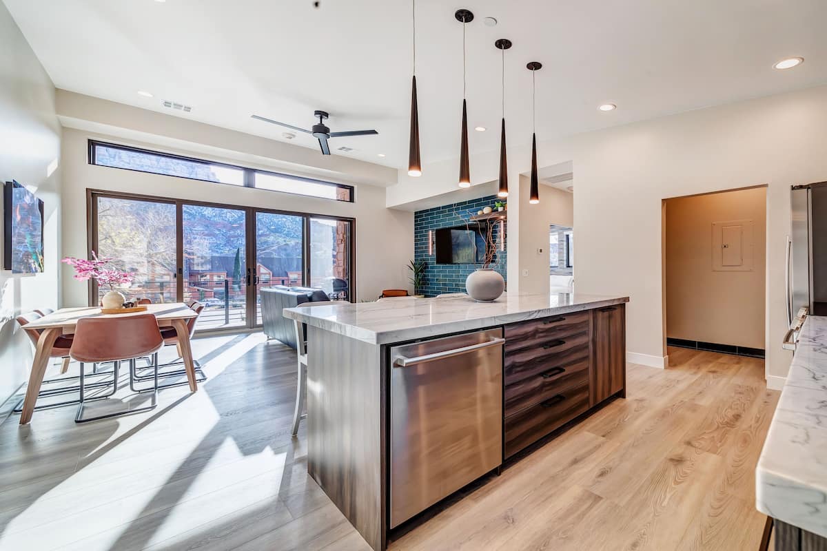 A modern kitchen with a central island, large windows, and a ceiling fan.