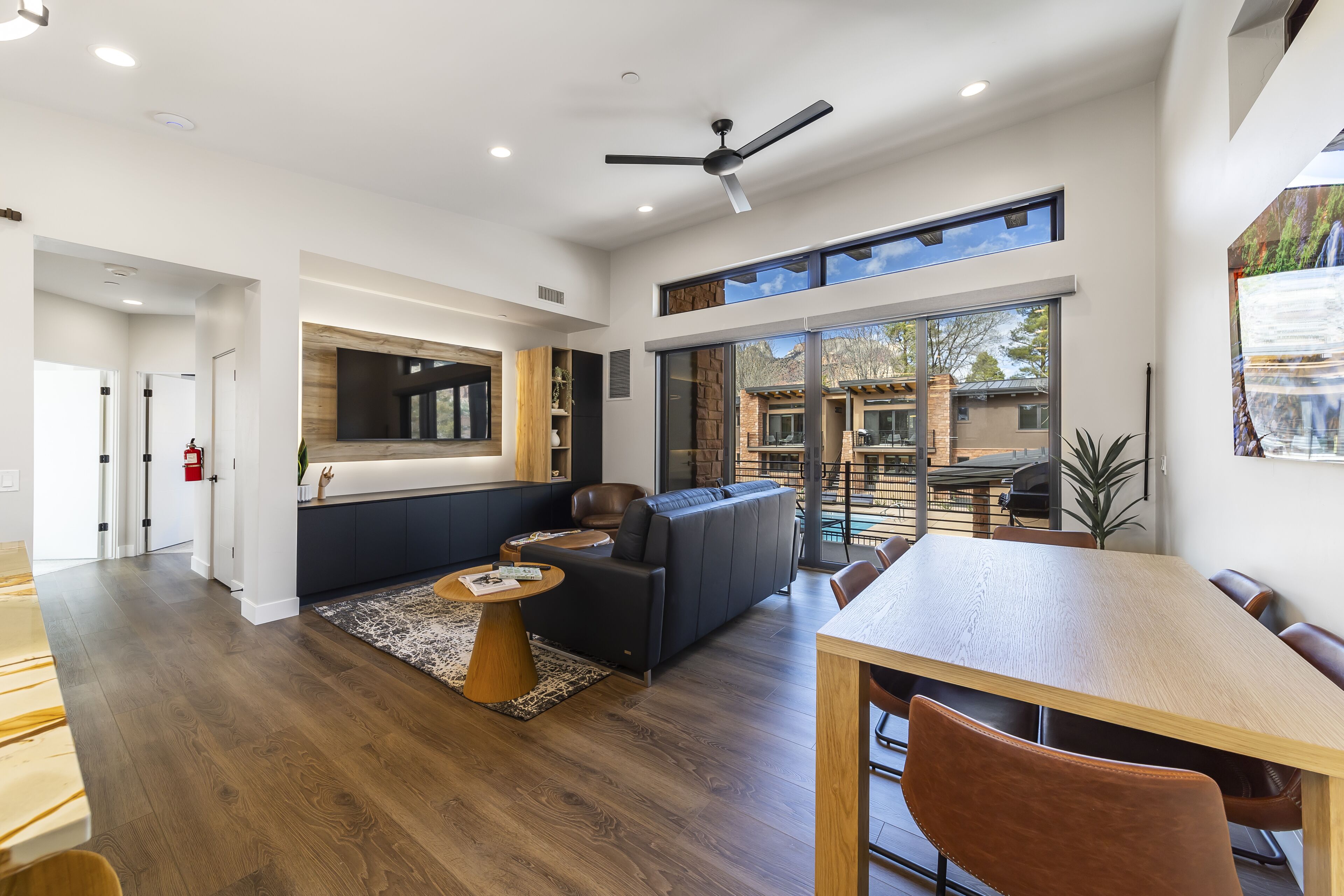 A spacious living area with a large window, a ceiling fan, and a dining table.