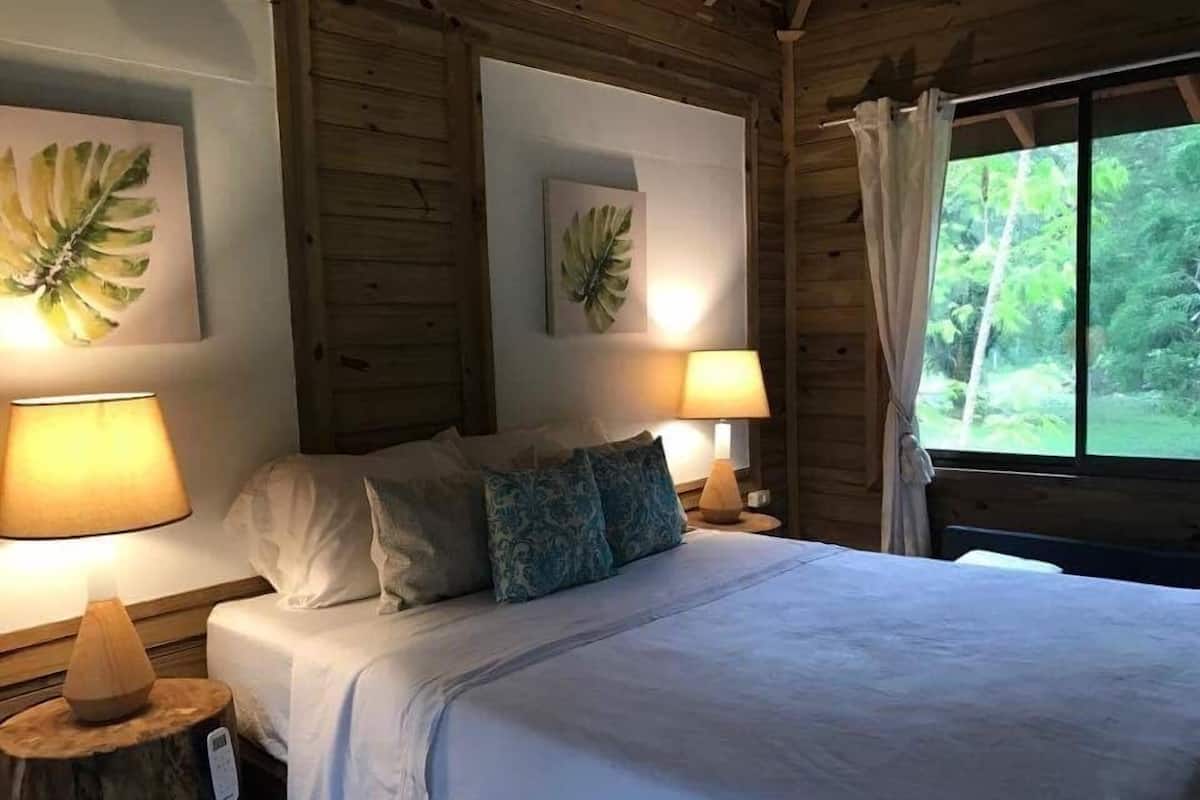 A wooden cabin bedroom with a bed, two wall-mounted lamps, and framed leaf artwork.