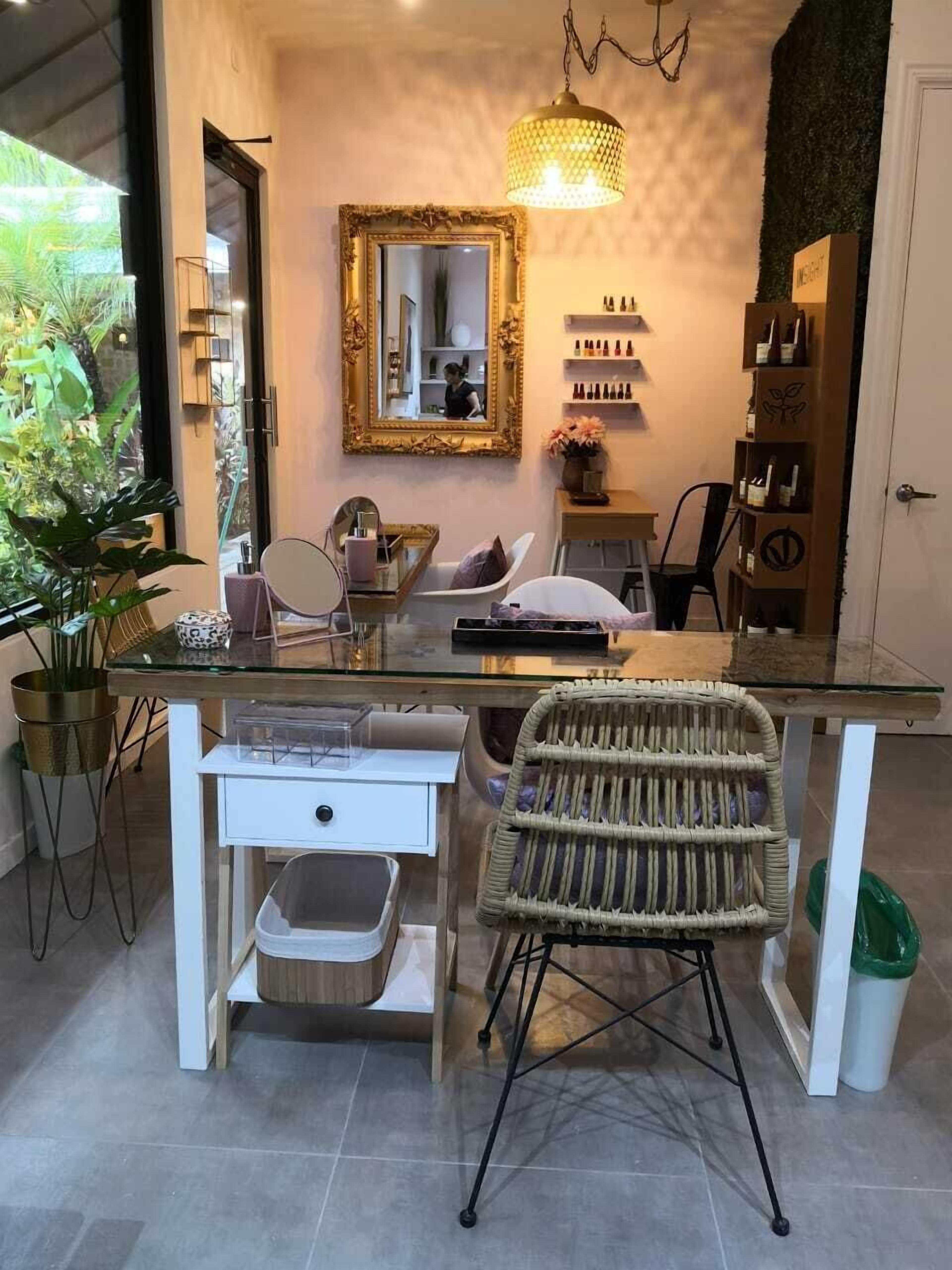 Un baño moderno con tocador de vidrio, una silla de mimbre, un espejo con marco dorado y una lámpara colgante.