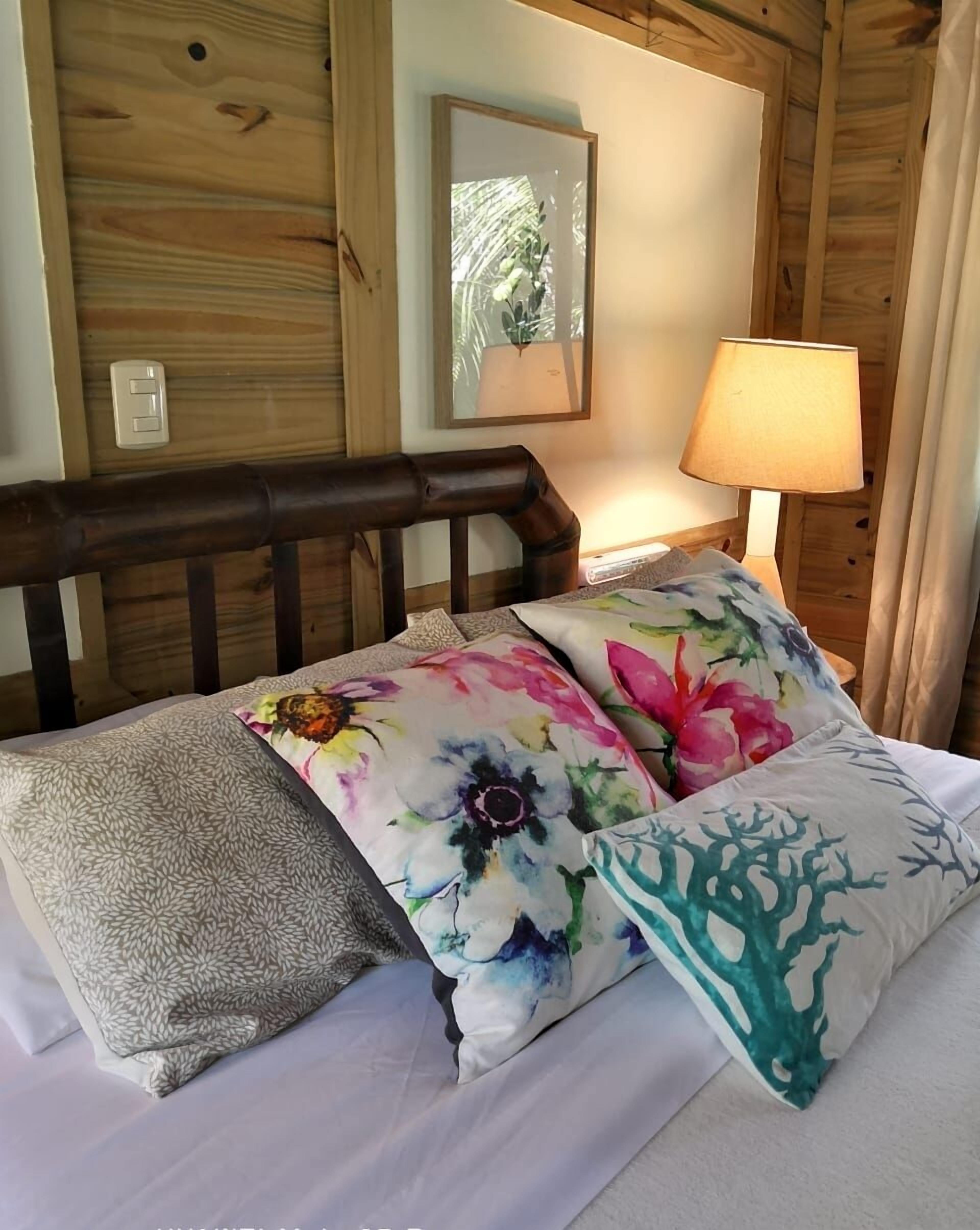 Ein holzgetäfeltes Zimmer im Chalet-Stil mit einem Bett, Kissen mit Blumenmuster, einer Lampe und einem Spiegel an der Wand.