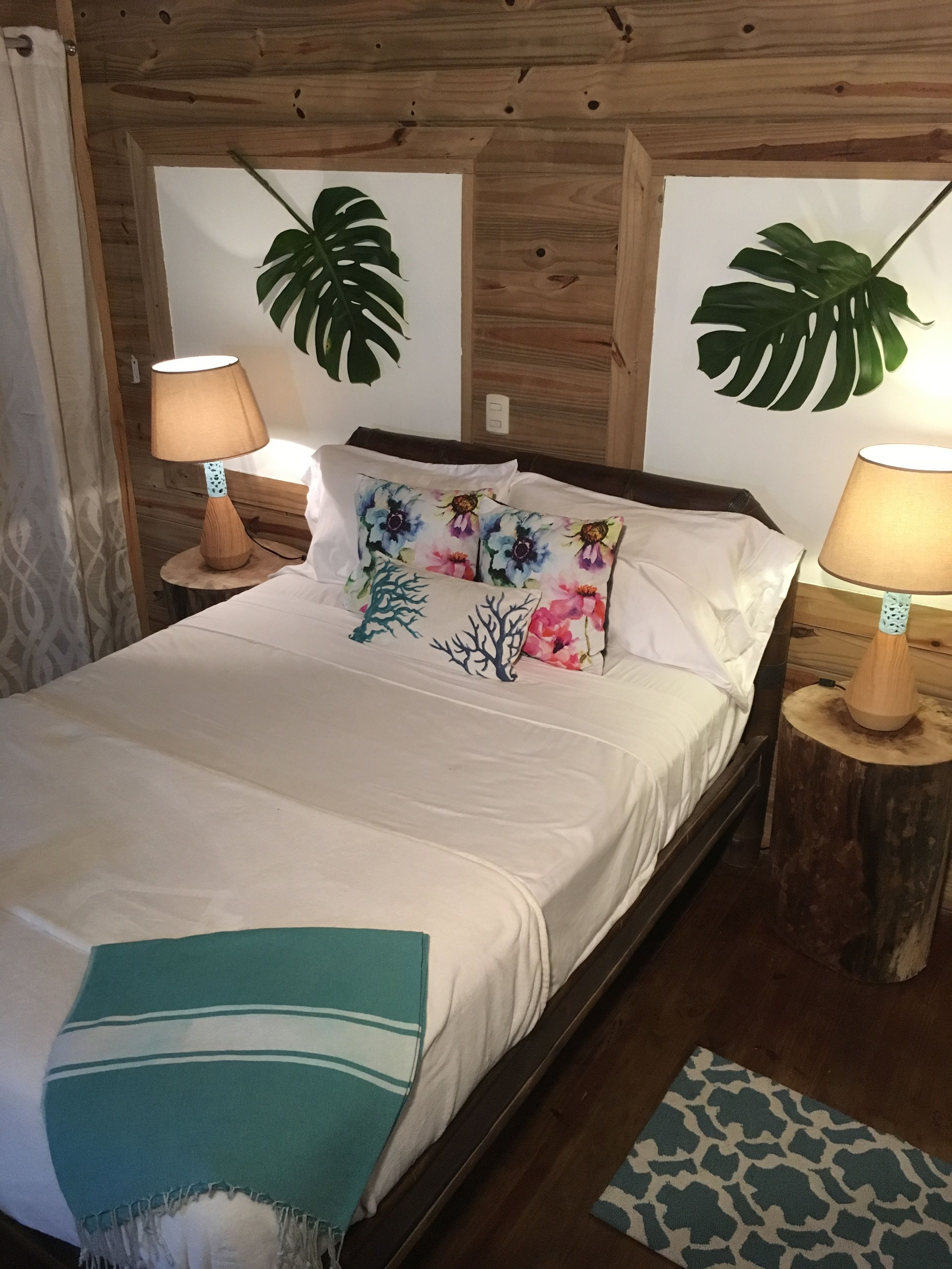 A bed with a white bedspread, two decorative pillows, a teal throw blanket, and two bedside lamps on wooden nightstands.