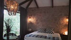 A bedroom with a large bed, a dining table with chairs, a chandelier, and a stone wall. - Boutique Hotel y Spa Tangara Azul (Ciudad Cortés)