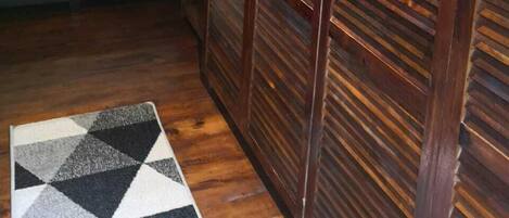 Un dormitorio con cama, armario de madera, alfombra geométrica e iluminación colgante.