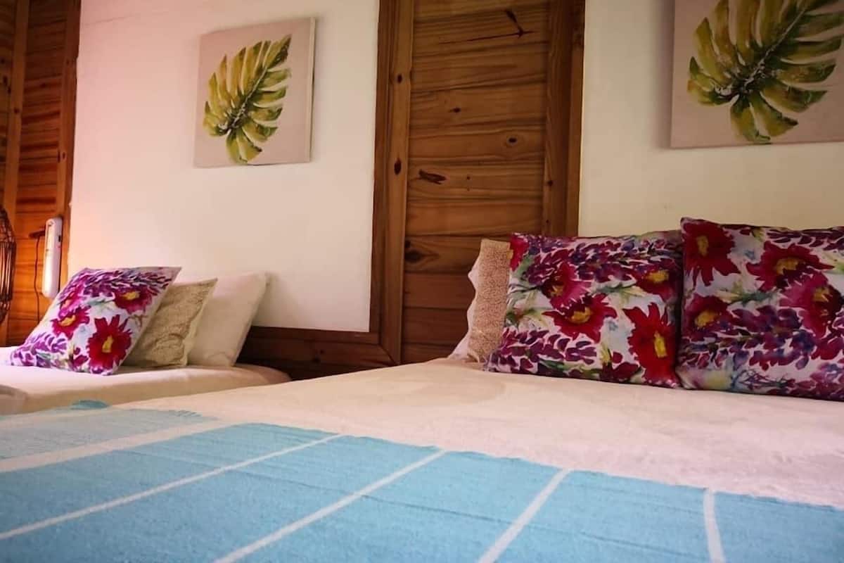 A bedroom with a bed, two pillows, a wooden door, and a wall with a leaf painting.