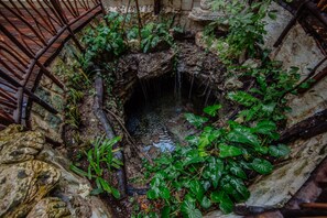 Ein kreisförmiges Steingebäude mit einem zentralen Wasserspiel inmitten üppiger Bepflanzung.