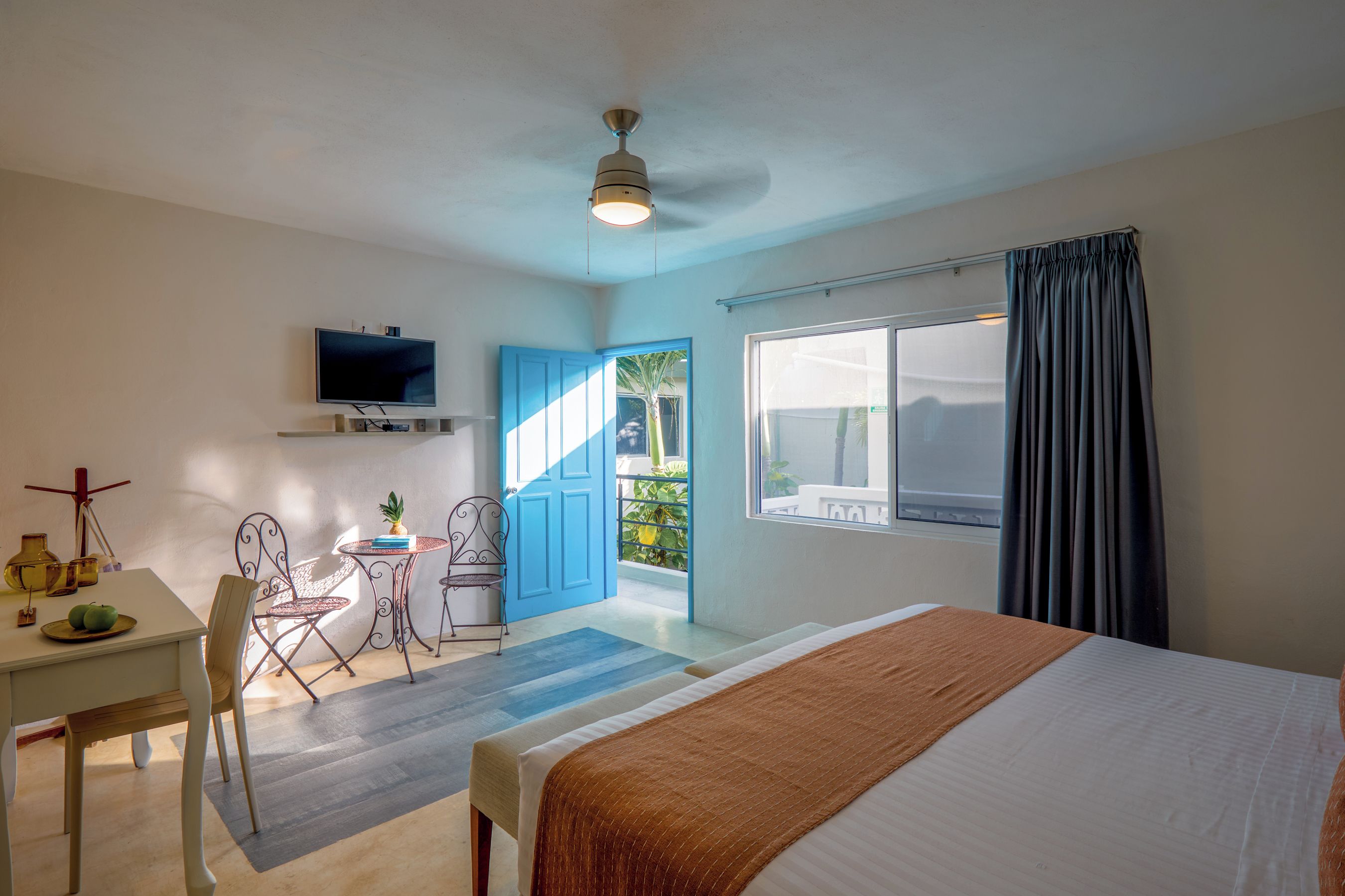 A hotel room with a bed, a desk with a TV, a chair, and a view of the outdoors.