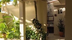 Un espacio interior iluminado por el sol, con plantas en macetas, suelo de baldosas y pared con diseño.