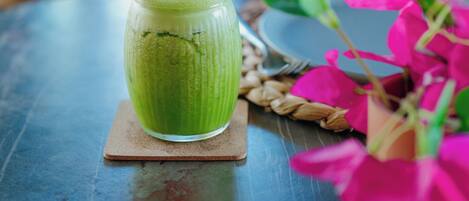 A green beverage in a glass on a coaster, a menu, and pink flowers on a table.
