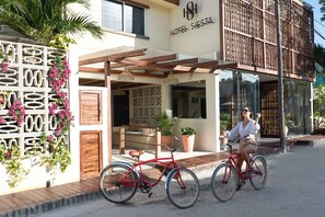 Entrada de un hotel con un porche cubierto, una bicicleta y una persona andando en bicicleta.