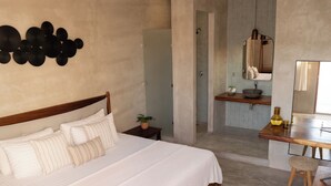 A bedroom with a large bed, a bedside table with a plant, a bathroom with a mirror and sink, and a wooden stool. - Hotel Siesta Holbox (Isla Holbox)