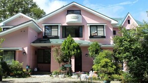 A pink two-story house with a front porch, a garage, and a small garden. - Pension AJIWAI (Nasu)