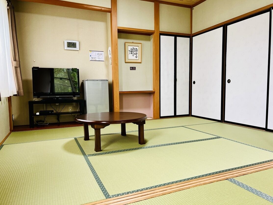 A tatami mat room with a television, a small table, and sliding doors.