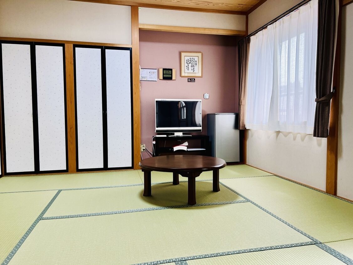 A traditional Japanese room with tatami flooring, a low table, a television, and sliding doors.