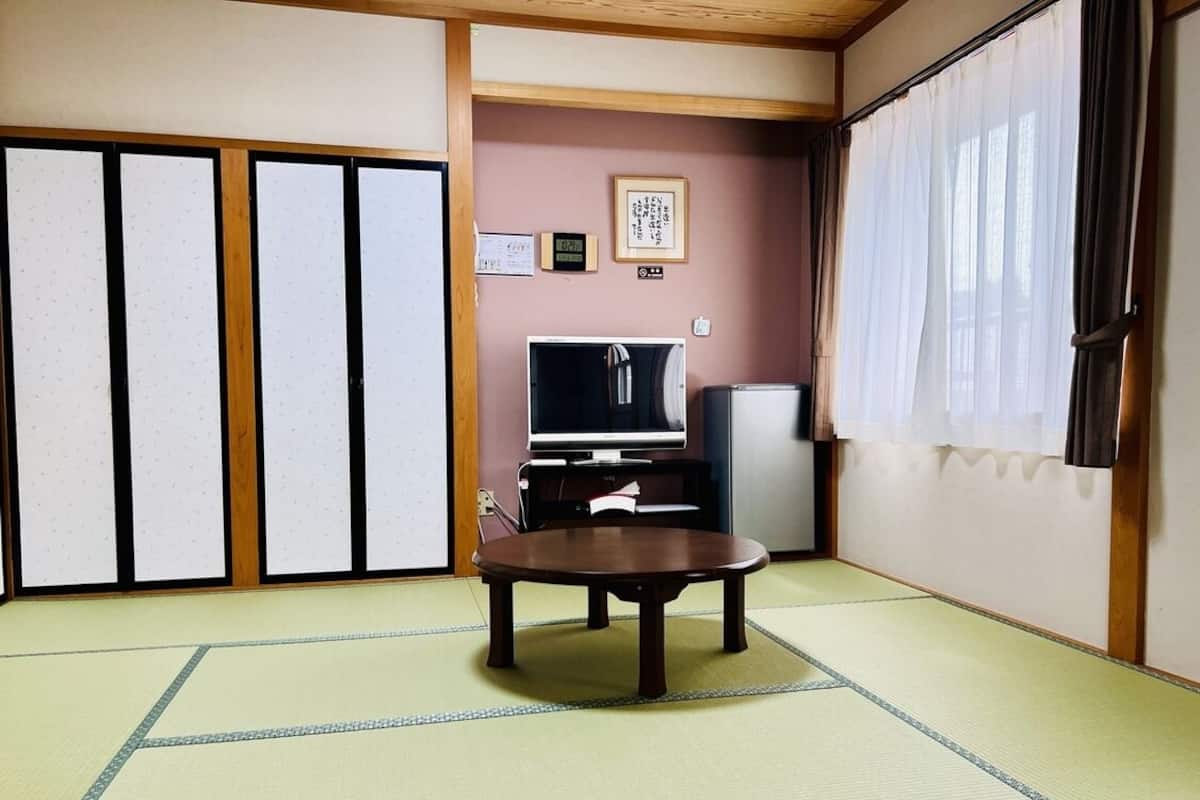 Ein traditioneller japanischer Raum mit Tatami-Böden, einem niedrigen Tisch, einem Fernseher und Schiebetüren.