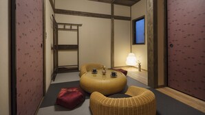 A traditional Japanese room with tatami flooring, a round woven table with cups, a low wooden bed, and a sliding door with a pattern. - Hanagoromo (Kyoto)
