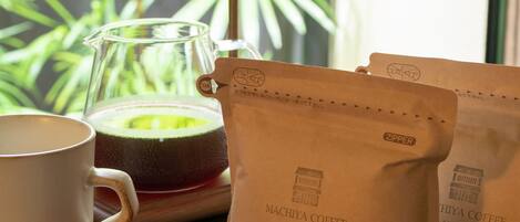 A coffee setup with a coffee maker, a glass carafe, and two bags labeled 'MACHIYA COFFEE'.