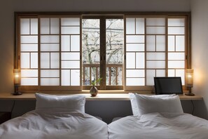 A hotel room with a large window, a bed with white bedding, a small table with a vase, and two lamps. - Hanagoromo (Kyoto)