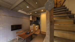 A modern kitchen with built-in appliances, a dining area with a wooden table and chairs, and a staircase with wooden steps. - Hanagoromo (Kyoto)