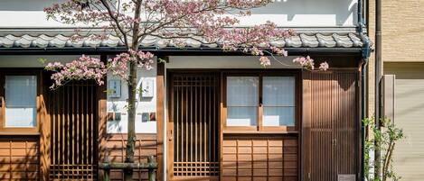 Un edificio japonés tradicional con puertas correderas de madera, techo de tejas y un cerezo en primer plano.