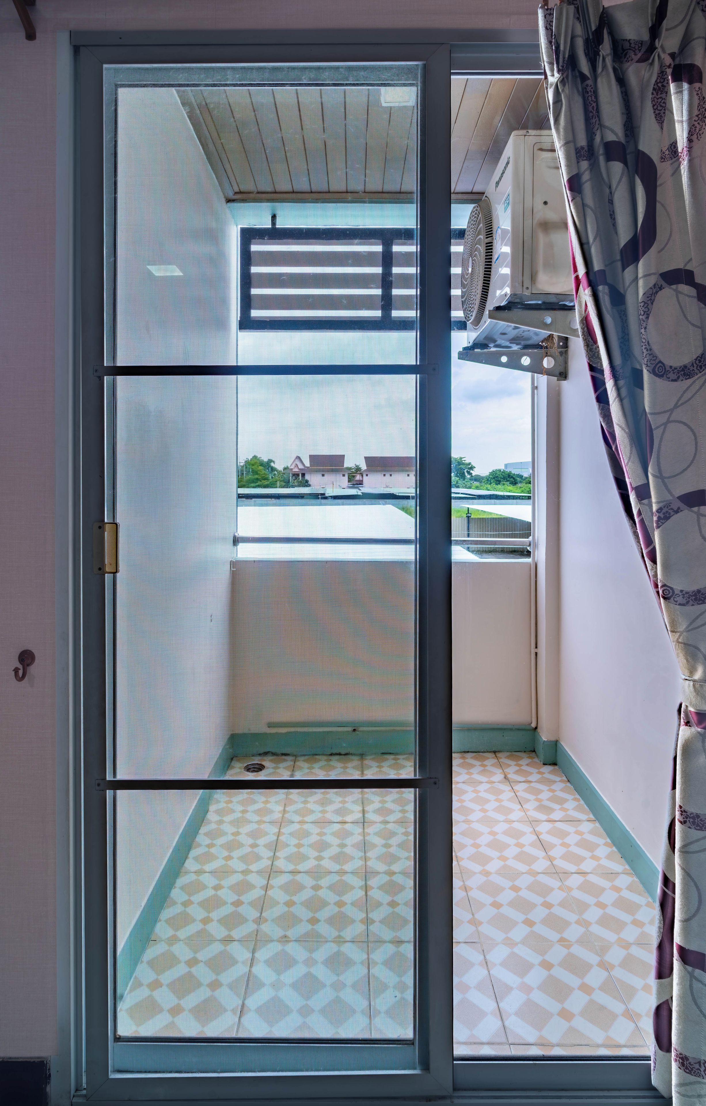Eine Schiebetür führt zu einem Balkon mit gemusterten Bodenfliesen und Blick auf Gebäude in der Ferne.