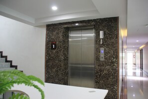 A modern elevator with a marble wall, a phone, and a digital display. - Gold Airport Suites (Bangkok)