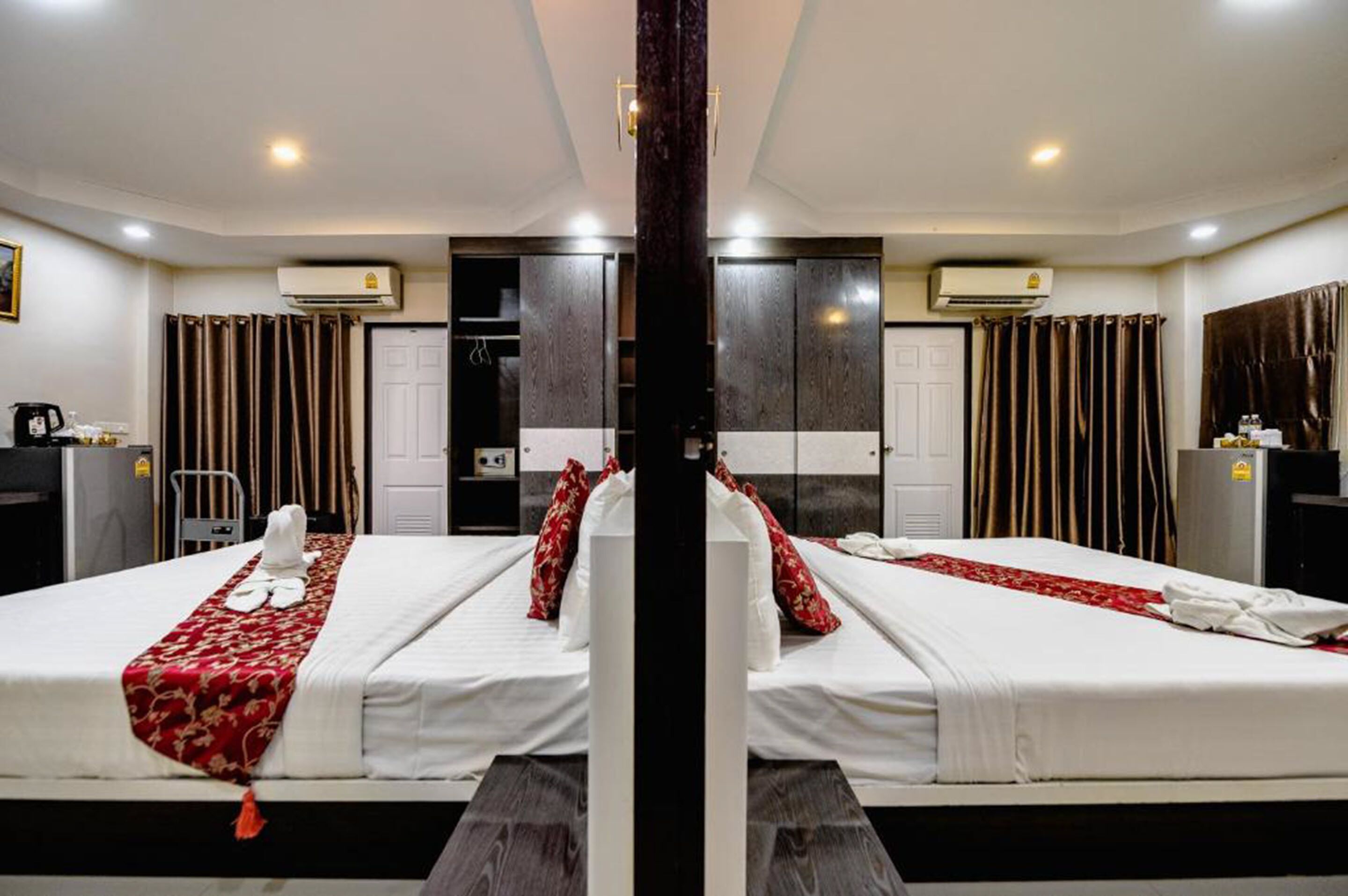 Une chambre d’hôtel aux murs recouverts de miroirs, avec deux lits, une colonne centrale et une armoire.