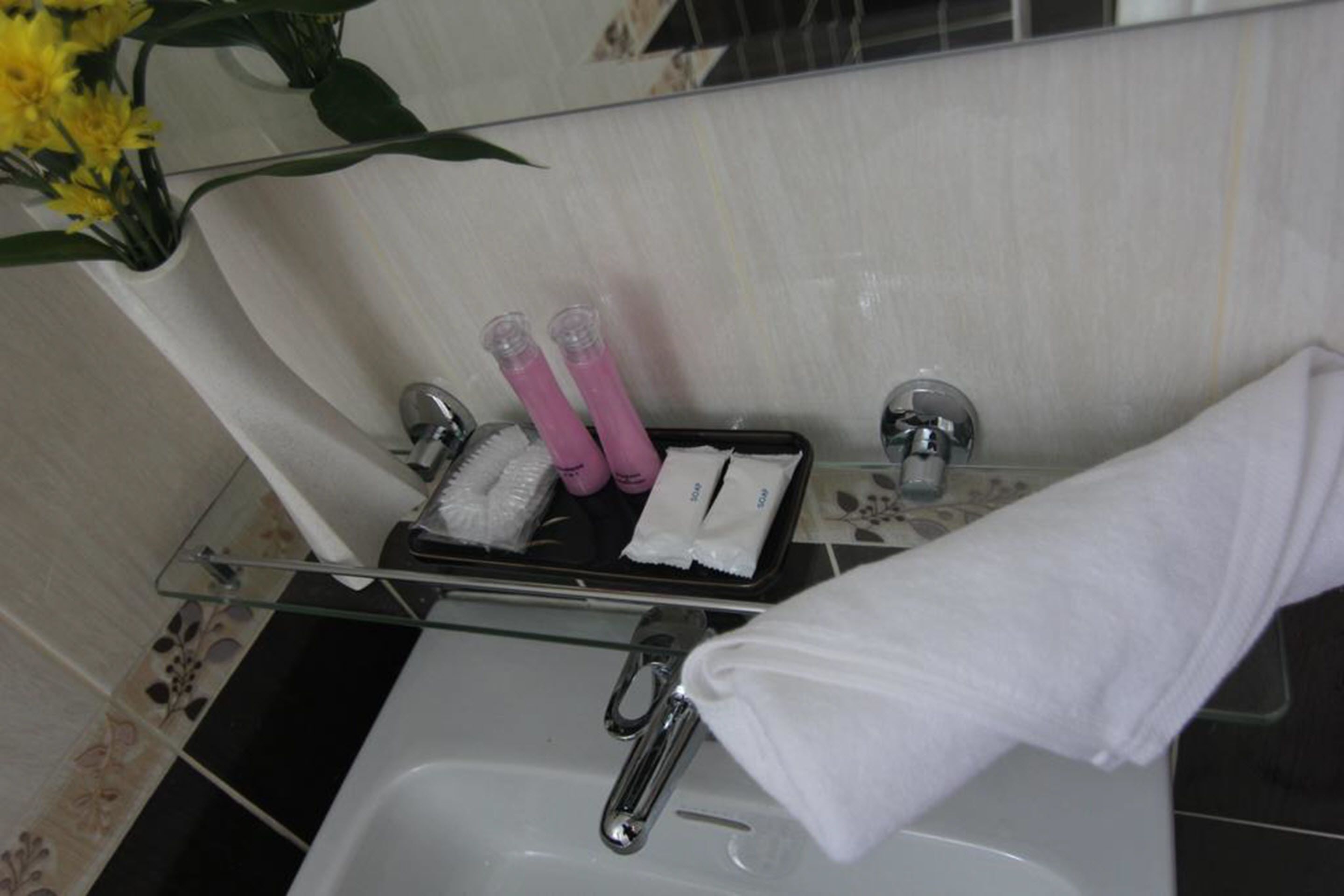 A bathroom with a glass shelf holding toiletries, a towel, and a flower arrangement.