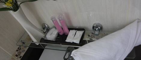 A bathroom with a glass shelf holding toiletries, a towel, and a flower arrangement.