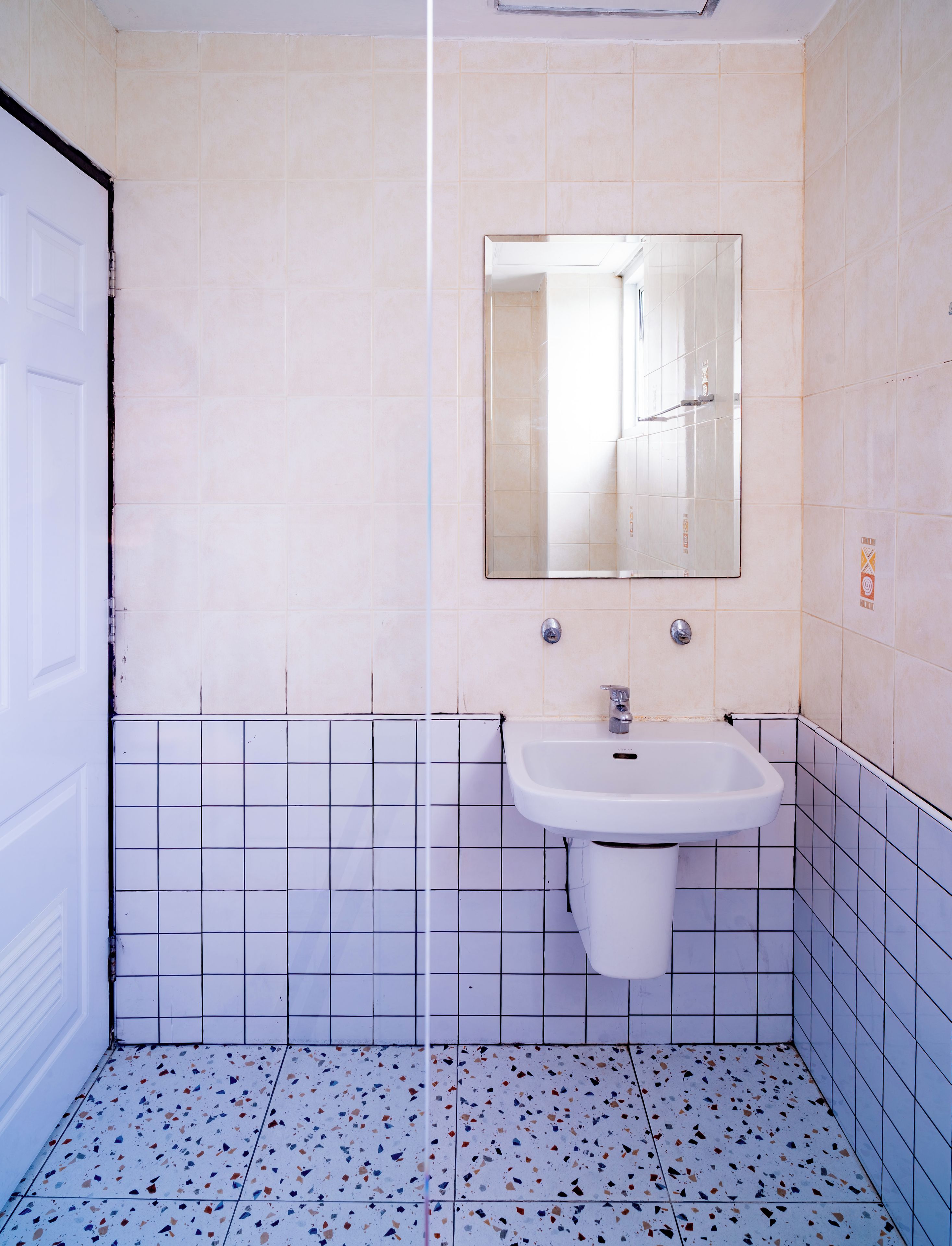 Une salle de bain avec un lavabo blanc, un miroir et une porte.