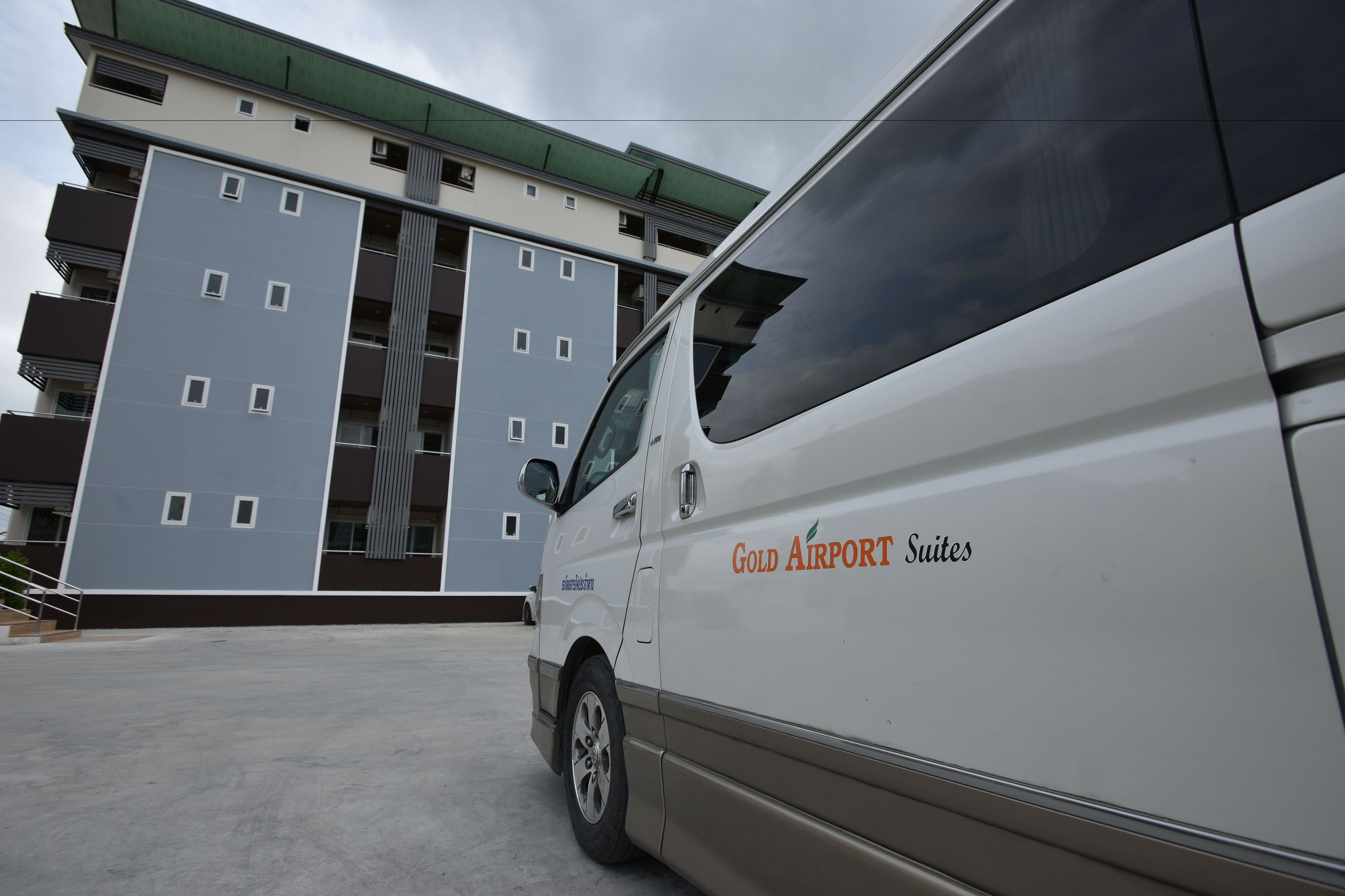 A white van parked in front of a building with multiple balconies and a green roof.