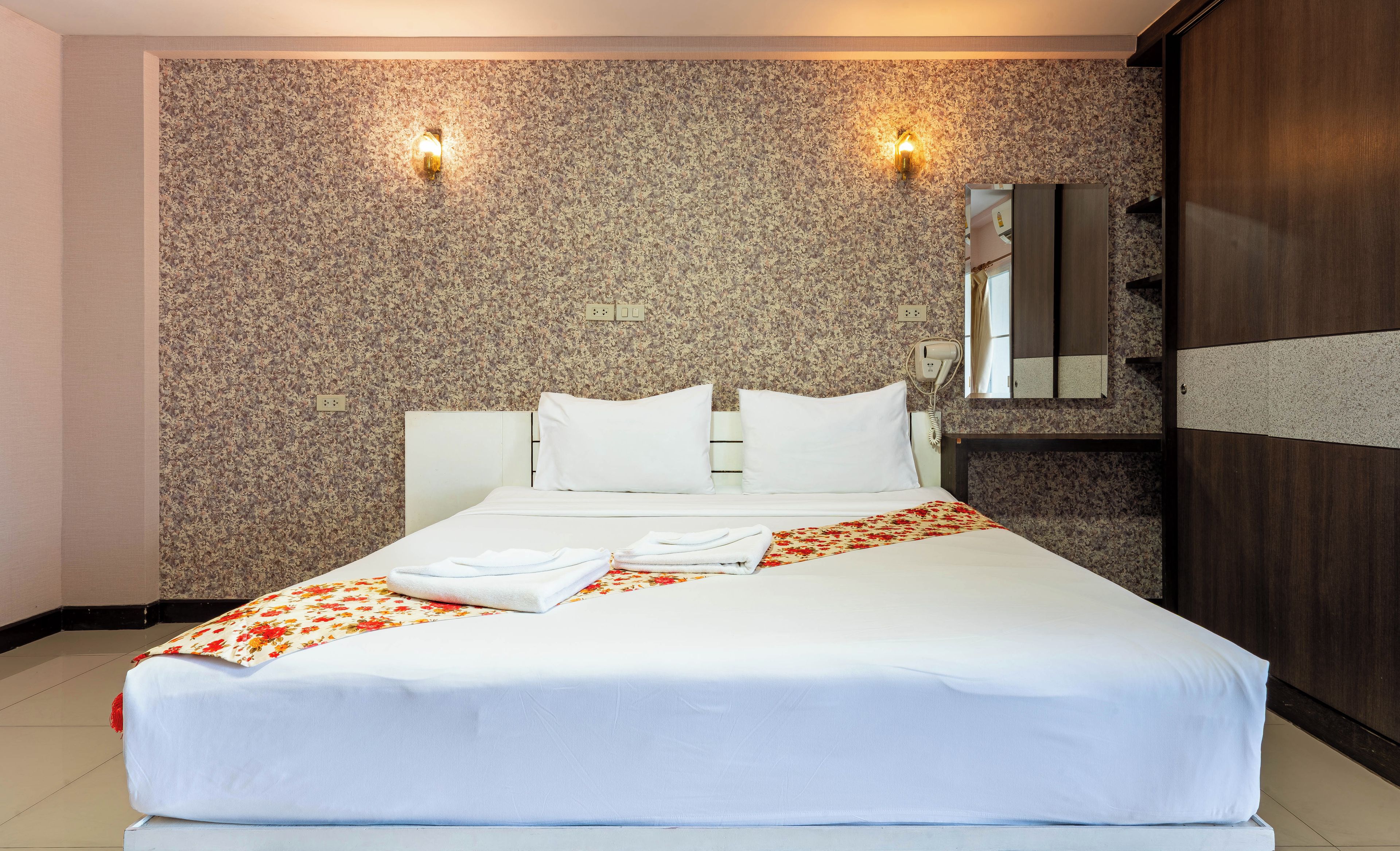 Une chambre d’hôtel avec un grand lit, deux lampes fixées au mur, un miroir et une armoire.