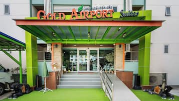 The entrance to a hotel named 'Gold Airport Suites' with a green awning and a ramp for accessibility.