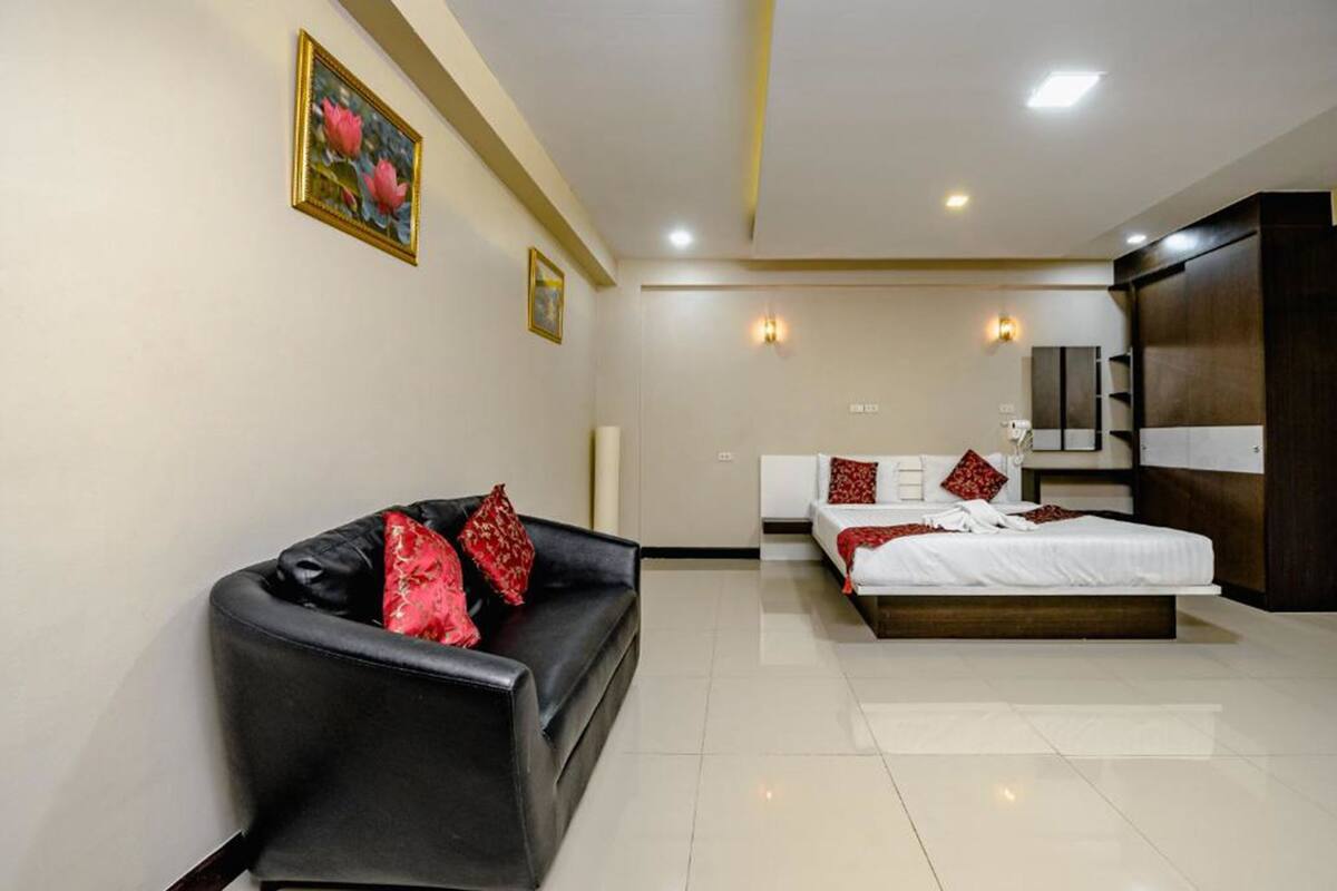 A modern hotel room with a black leather sofa, a large bed with white bedding, and a wooden wardrobe.