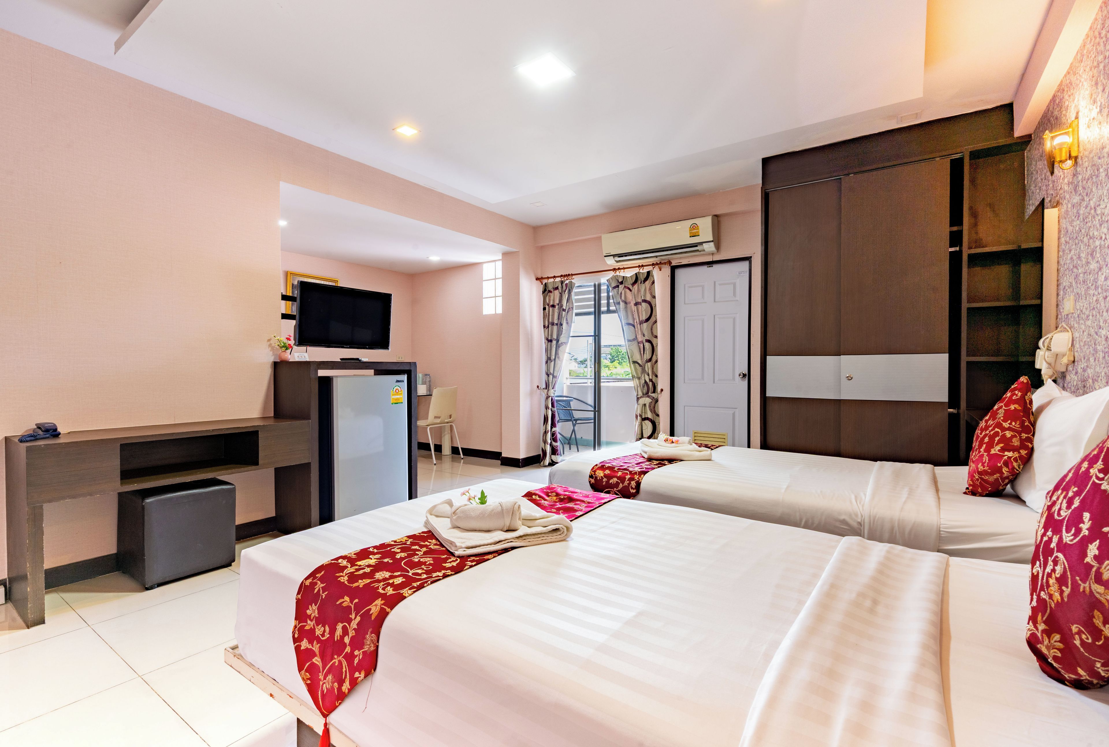 A hotel room with two beds, a desk with a television, a minibar, and an air conditioning unit.
