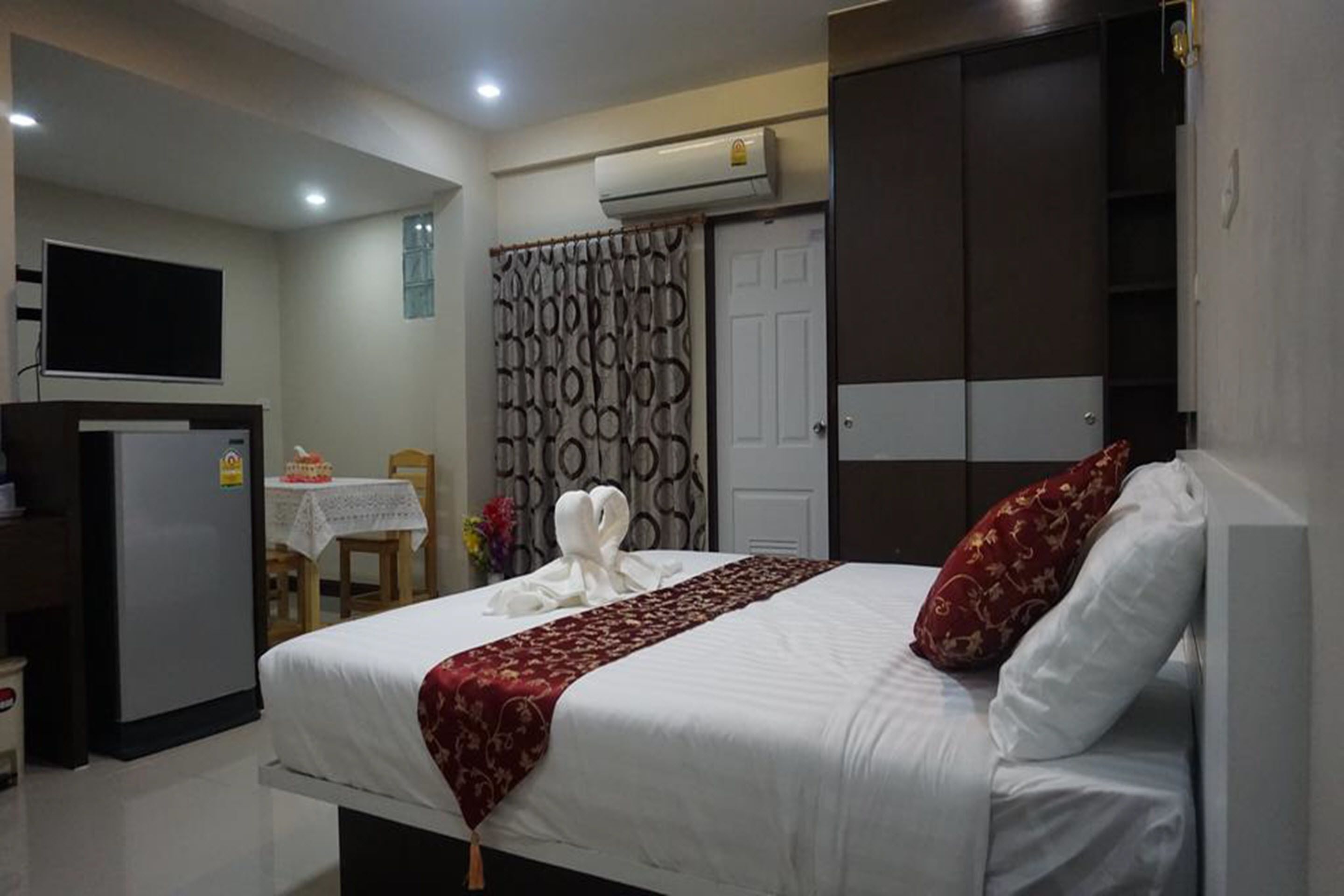 A hotel room with a bed, a television, a desk with a chair, and an air conditioning unit.