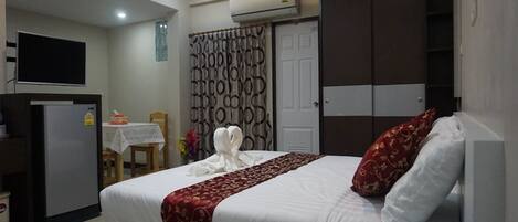 A hotel room with a bed, a television, a desk with a chair, and an air conditioning unit.