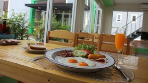 Una mesa de desayuno con un plato de huevos, tocino, jamón y verduras, un vaso de jugo de naranja, y un tenedor y un cuchillo.