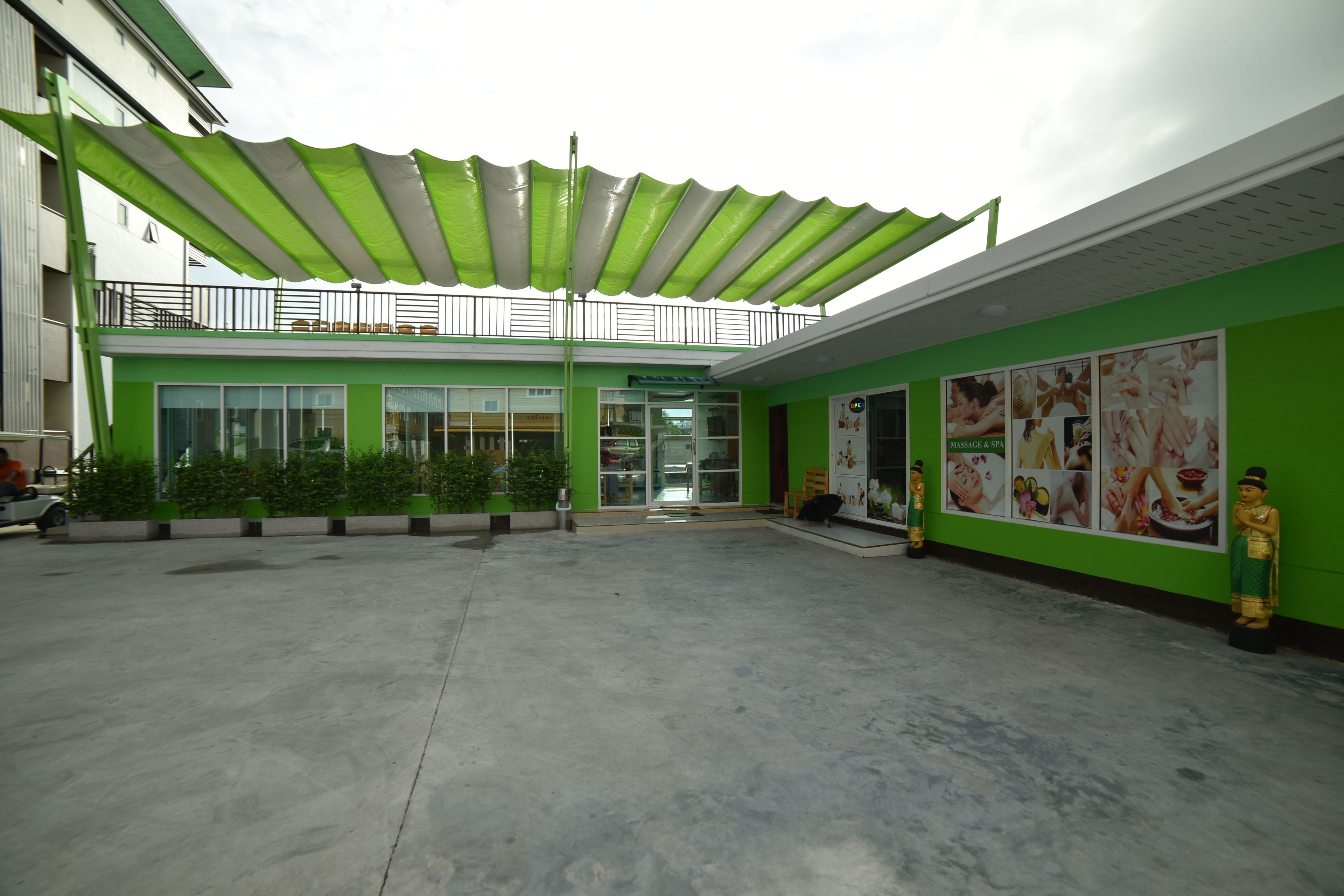 A building with a green exterior, a covered outdoor area with a concrete floor, and a sign for a massage and spa service.