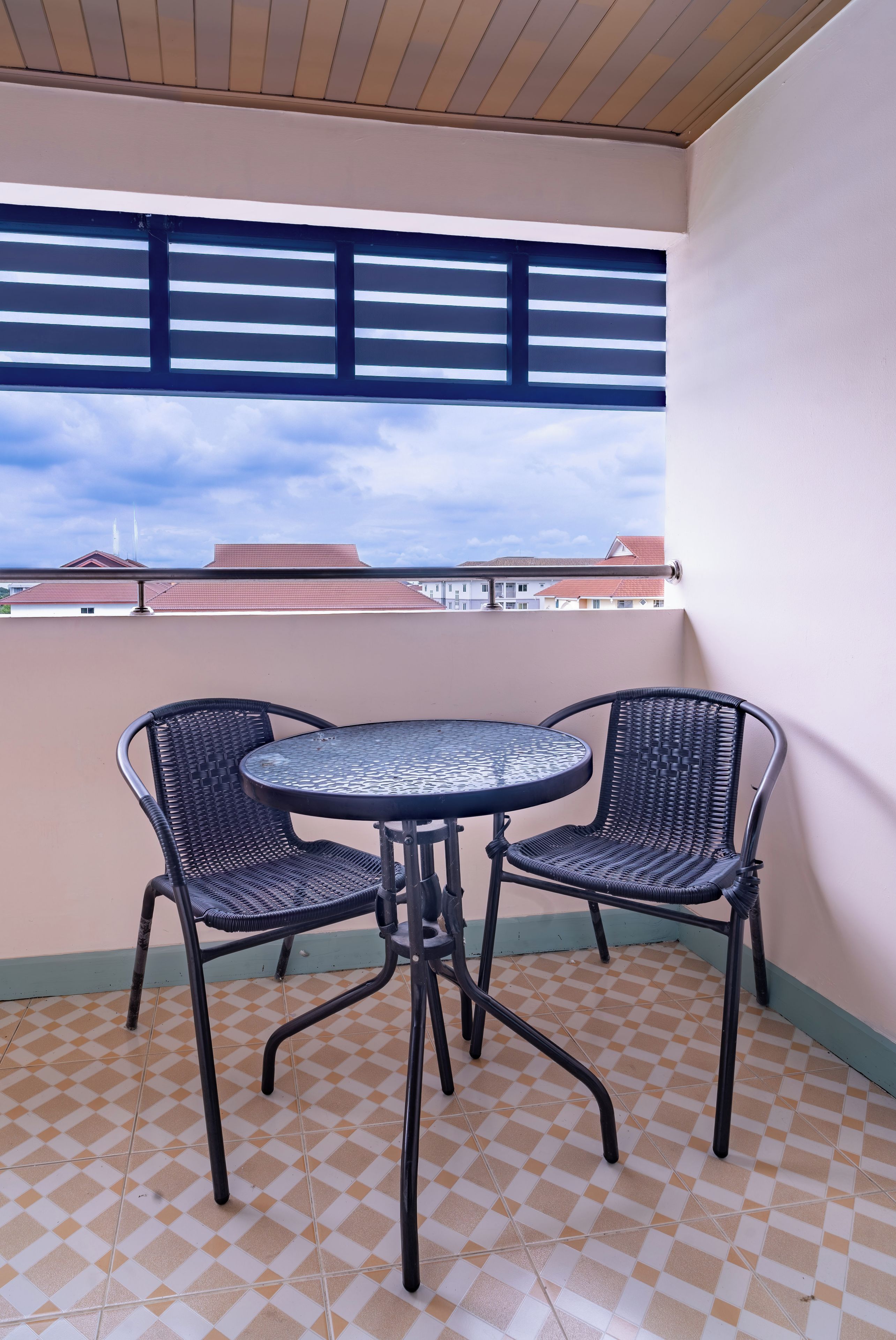 A balcony with a checkered floor, two wicker chairs, and a round metal table.