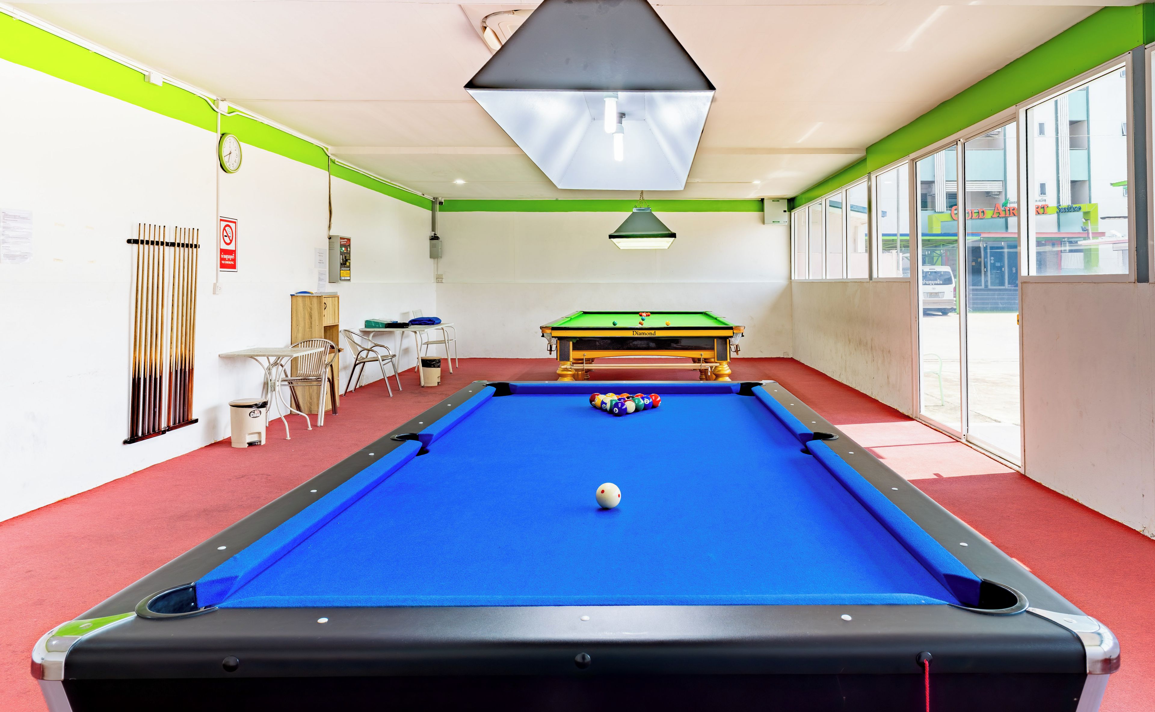 A pool table with a blue felt surface, a clock on the wall, and a window with a view of the outside.