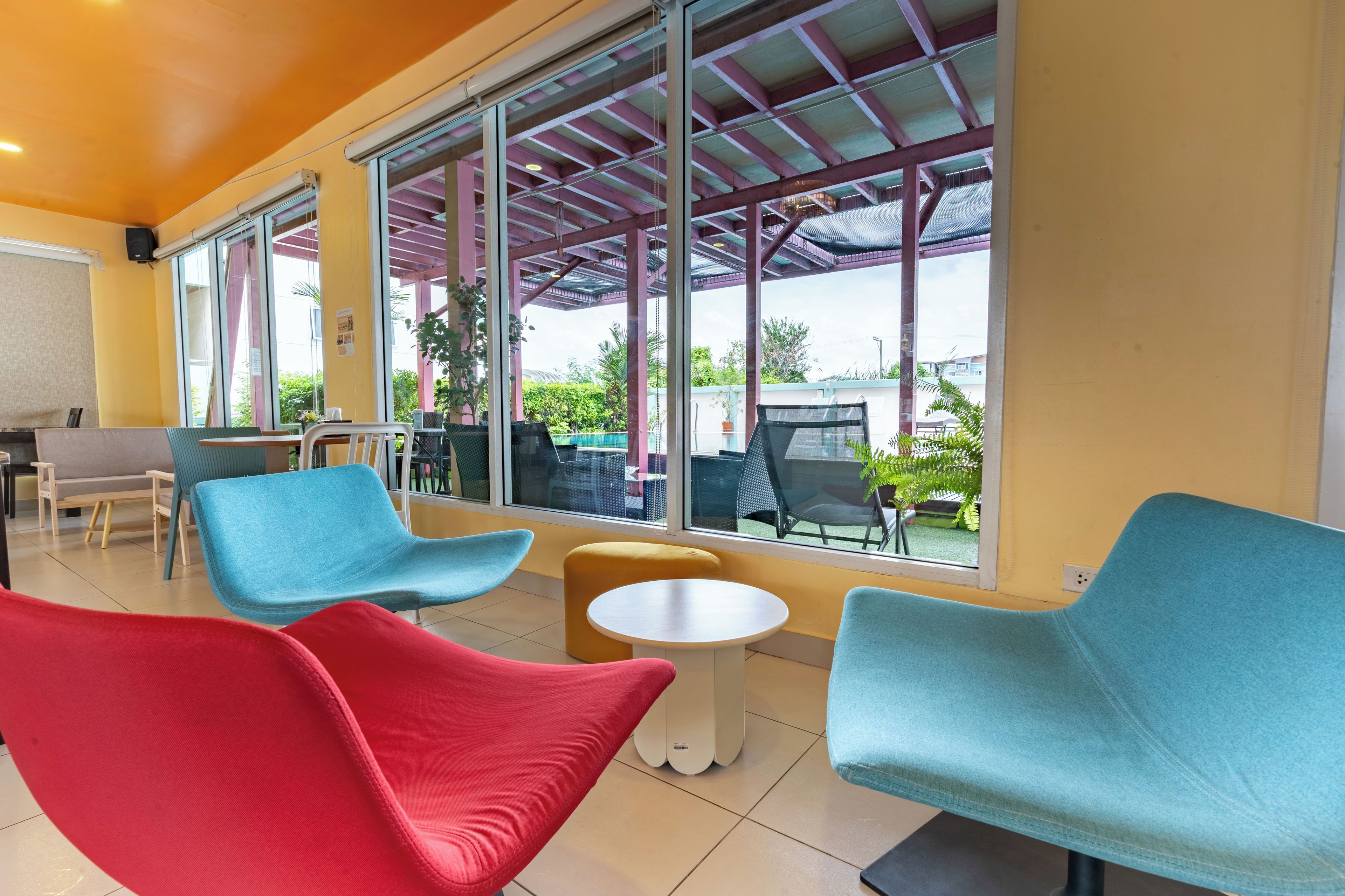 A modern interior with a seating area featuring blue and red chairs, a small round table, and large windows offering a view of the outdoors.
