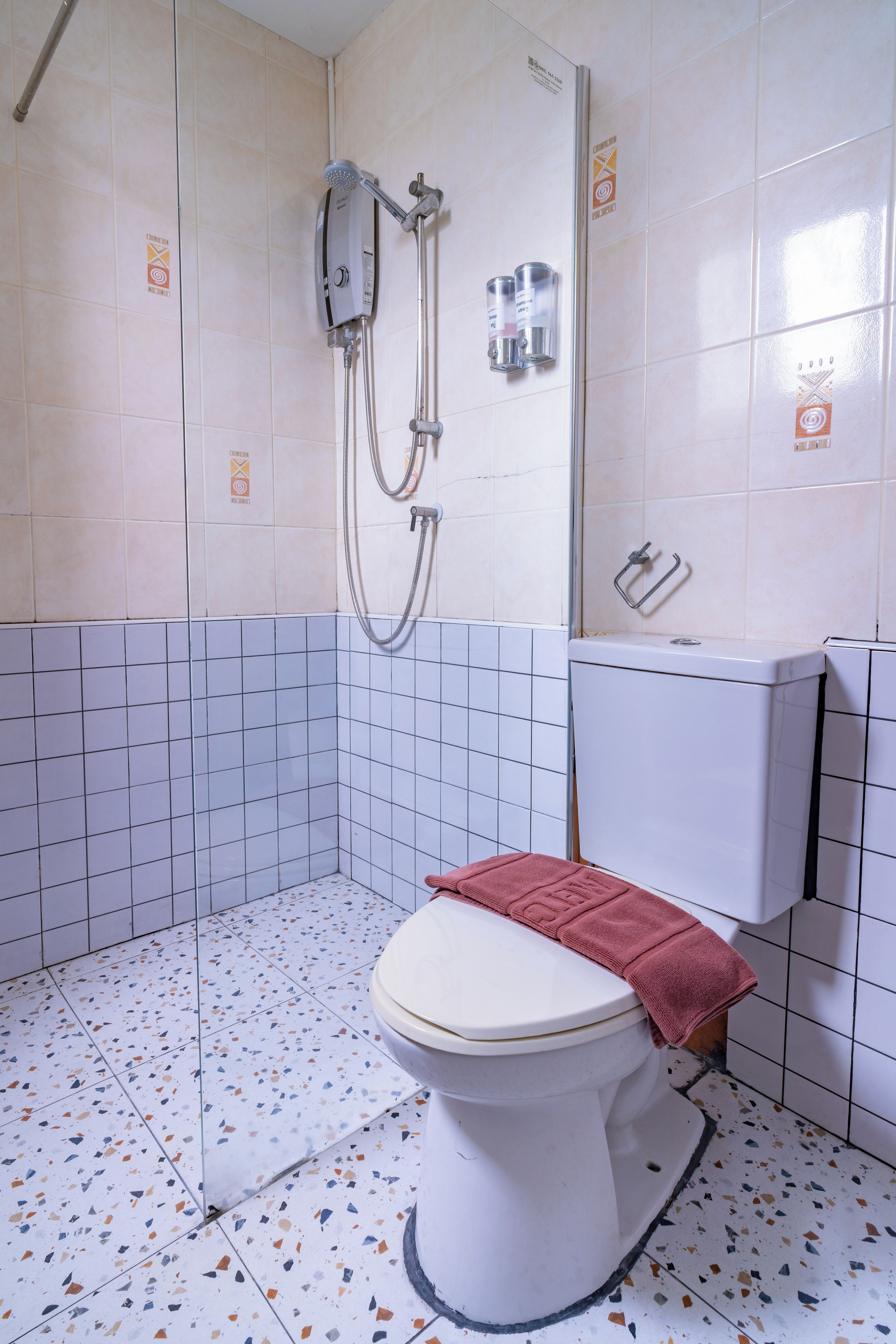 A bathroom with a white toilet, a shower with a handheld showerhead, and a wall-mounted soap dispenser.