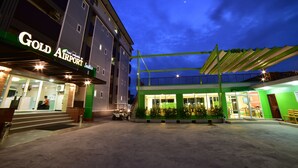 Un hotel con un llamativo letrero que dice "Gold Airport Suites", un área exterior cubierta y una escalera que conduce a la entrada.