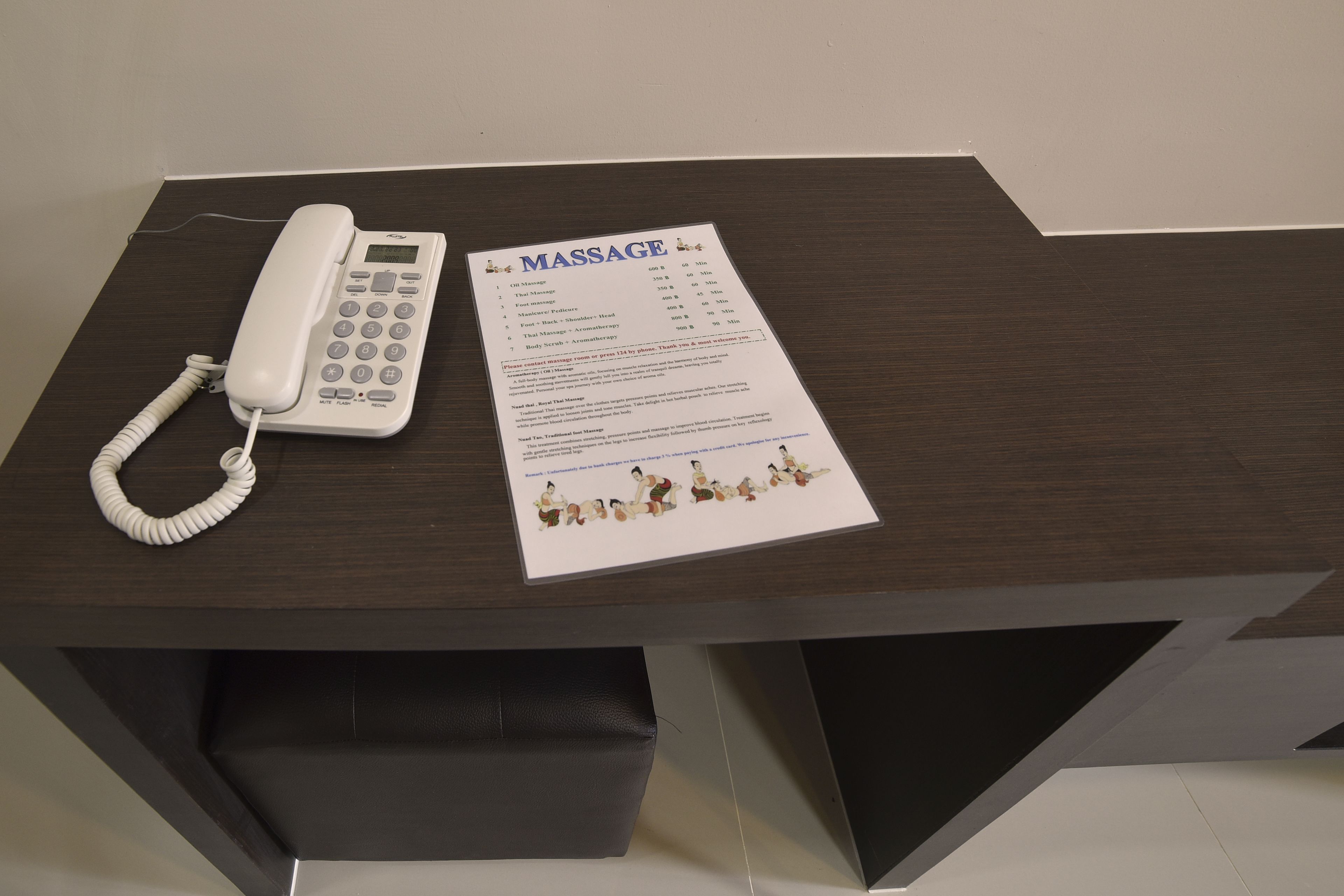 A desk with a white telephone and a massage service brochure.