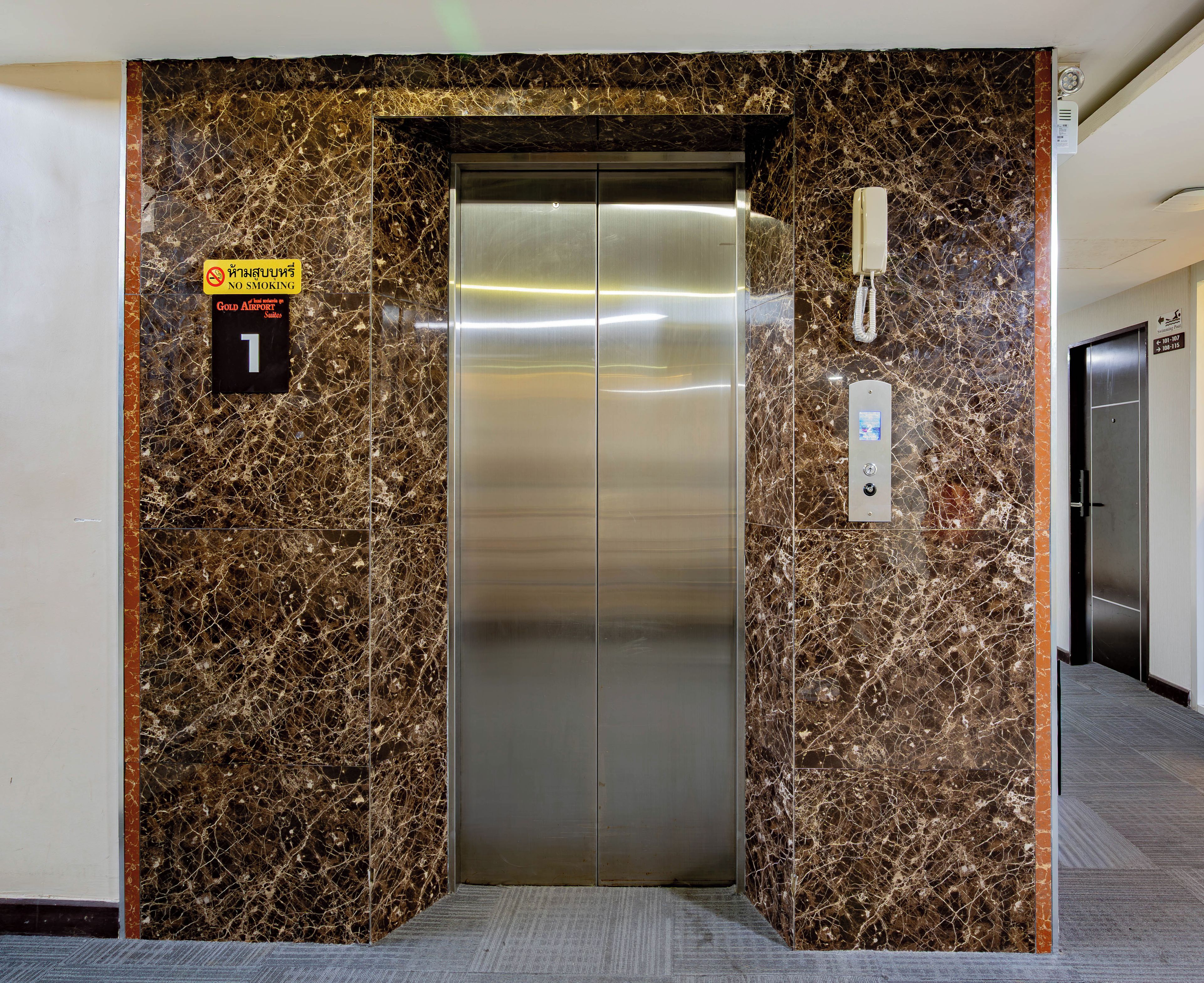 An elevator with a marble wall, a no-smoking sign, and a phone.