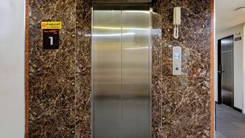 An elevator with a marble wall, a no-smoking sign, and a phone.