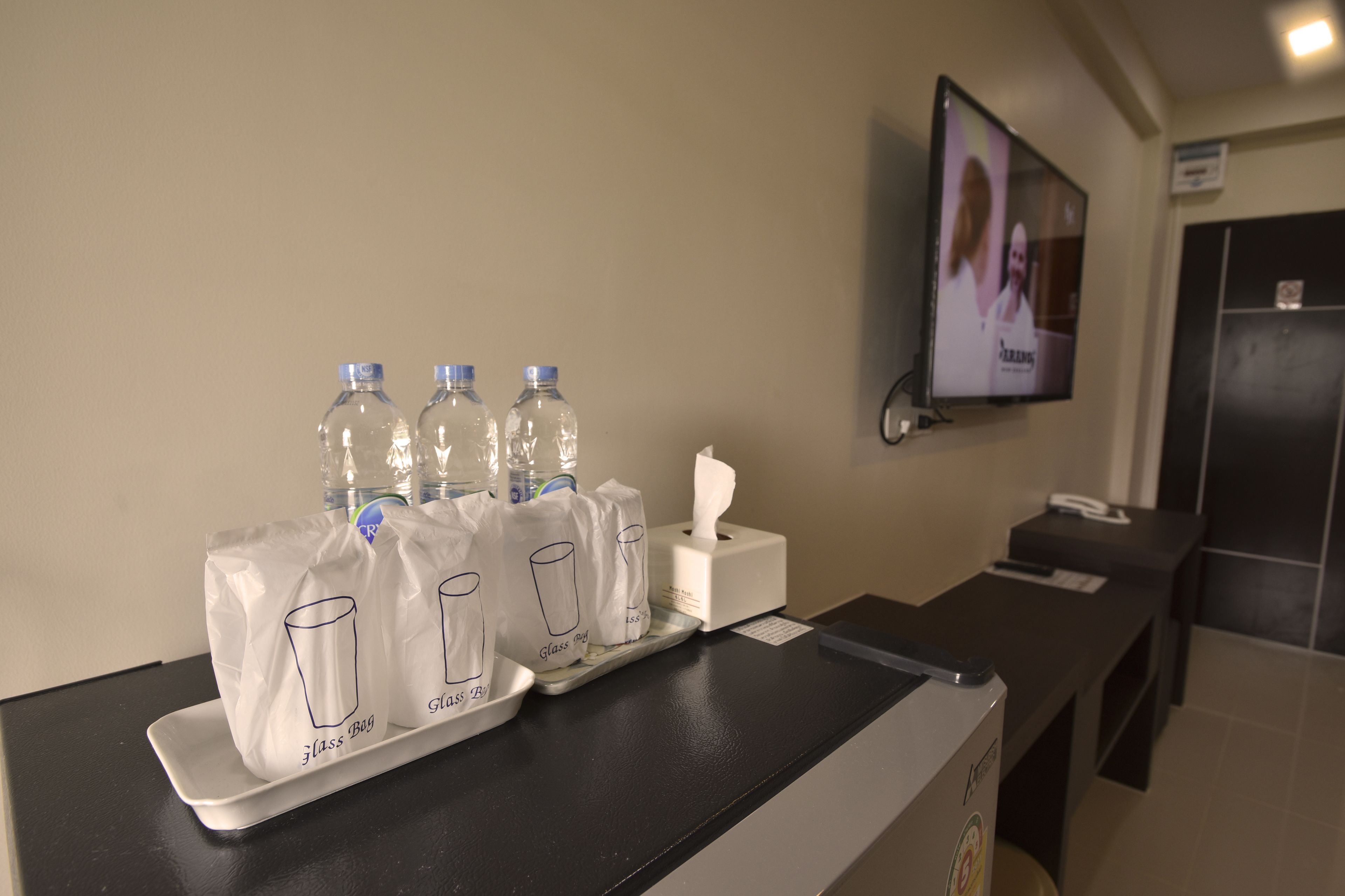 Un espace d’accueil comprenant un comptoir, des bouteilles d’eau, des sacs en verre, un distributeur de mouchoirs et un écran de télévision.